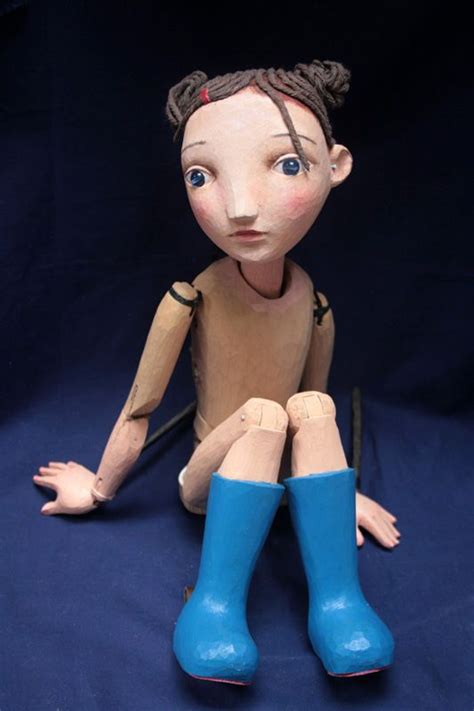 A Wooden Doll Sitting On The Ground Wearing Blue Boots And Holding A