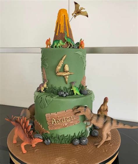 A Dinosaur Themed Birthday Cake With Dinosaurs On The Top Tier And An