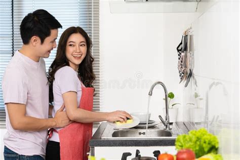 Happy Couple Washing Dishes Together In The Sink In The Kitchen At Home Man Is Hugging Woman