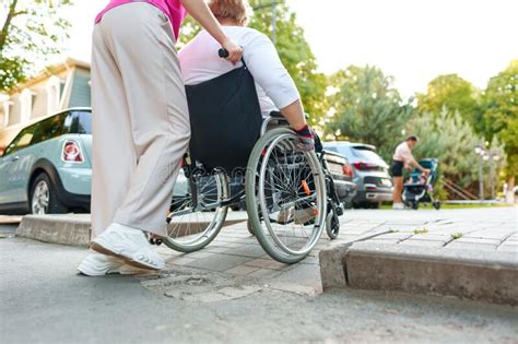 Young Female Caregiver Pushing Wheelchair With Female Person With