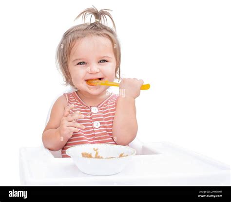 Baby Sitting In Chair And Eating Porridge With Spoon Isolated On White