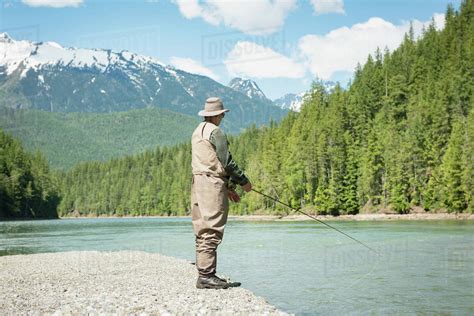 Full Length Of Man Fishing In River While Standing On Riverbank Against