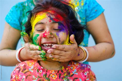 mother smearing color powder on her daughters face during holi celebration portrait del