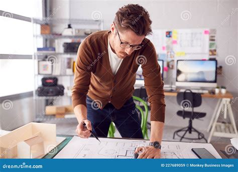 Male Architect Standing At Desk In Office Amending Building Plans Stock