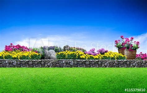 Flower Garden Green Grass And Stone Fence On Blue Sky Background