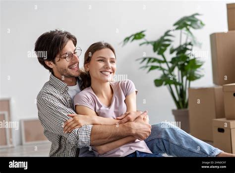Glad Caucasian Millennial Man Hug Lady Sit On Floor With Cardboard Boxes Celebrate Moving