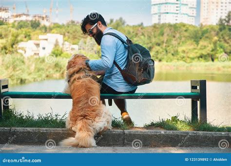 Young Man Sitting With His Dog On The Chair In The Park Hugging Stock