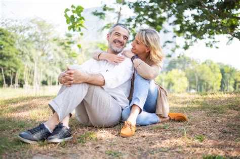 Caucasian Couple Sitting On Grass Together At Park Stock Photo By