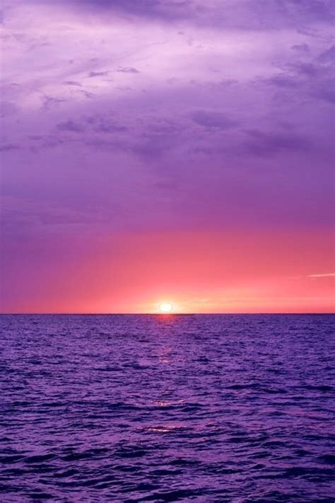 The Sun Is Setting Over The Ocean With Purple Hues In The Sky And Water