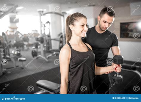 Woman Doing Bicep Curls In Gym With Her Personal Trainer Stock Photo