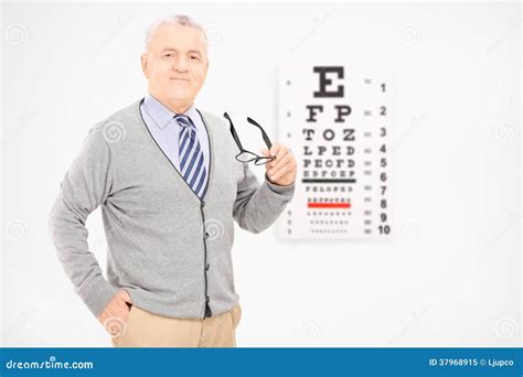 Mature Man Holding A Pair Of Glasses In Front Of An Eye Chart Stock