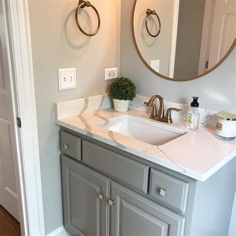 The kitchen island with a white quartz countertop blends perfectly with the soft tone of the beige floor and the functional black pedestal gray barstool. Powder Bathroom #graycabinets Dorian Gray Cabinets, Repose ...