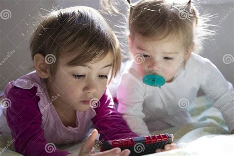 4 Year Old Girl And 1 Year Old Girl Laid In Bed Watching Tablet Stock