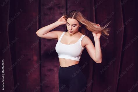 Sexy Blonde Woman With Huge Breast In A White Tank Top Standing On A Dark Wooden Wall Background