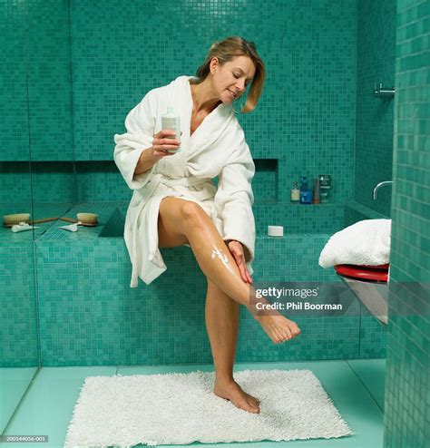 mature woman sitting on edge of bath applying cream to leg photo getty images