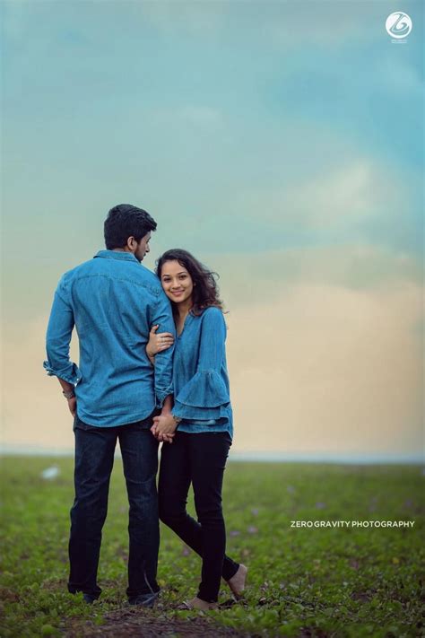A Man And Woman Are Standing In The Grass With Their Arms Around Each