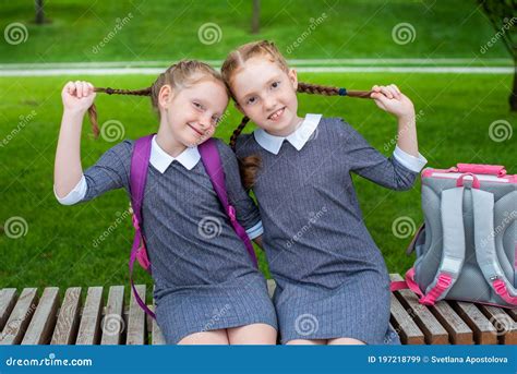 Two Cute Schoolgirls Are Sitting On A Bench And Smiling The Sisters Are Happy To Go Back To