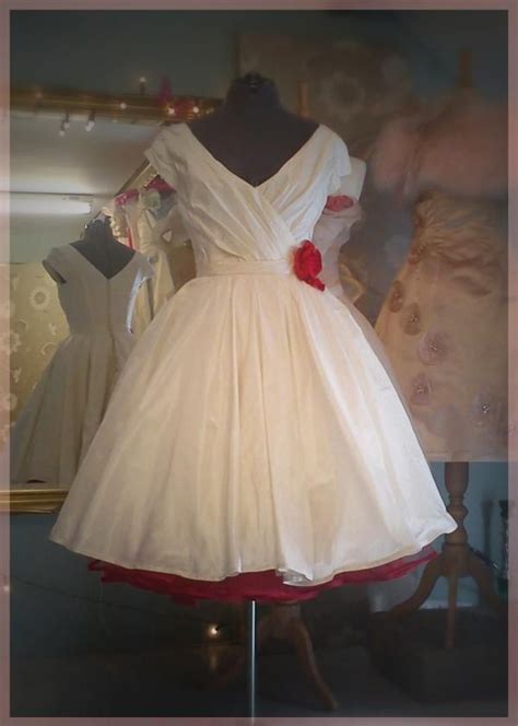 A White Dress On Display In Front Of A Mannequin Wearing A Red Bow