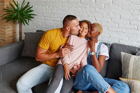 Mom And Dad Kissing Their Smiling Daughter By Stocksy Contributor