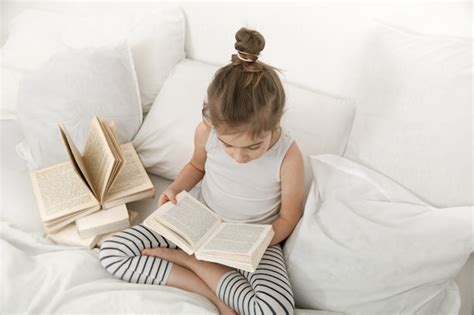 Cute Little Girl Reading A Book On The Bed In The Bedroom Free Photo