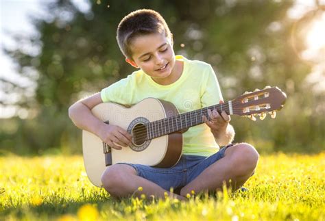 Niño Tocando Guitarra Acústica En Un Campo Al Atardecer Foto De Archivo