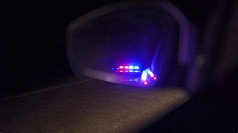 Flashing Police Lights Reflected In The Rearview Mirror Of A Car At