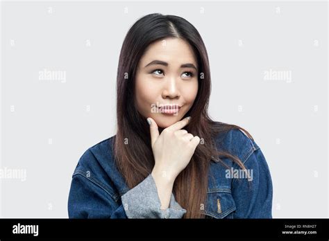 Portrait Of Dreamy Smiley Beautiful Brunette Asian Young Woman In Casual Blue Denim Jacket With