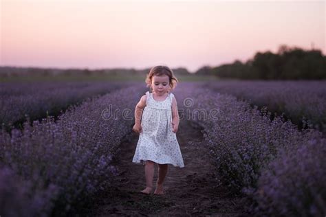 Little Girl In Flower Dress Runs Barefoot Across Field Of Purple