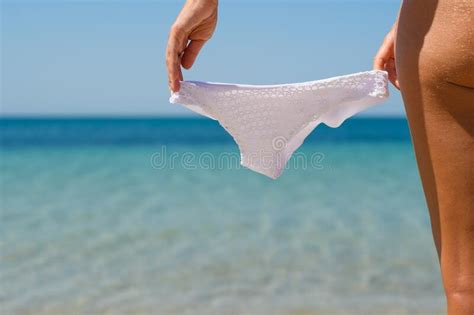 White Swimsuit In The Hands Of A Girl Against The Background Of An Empty Wild Beach And Sea