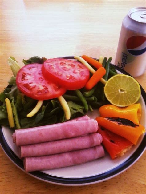 A White Plate Topped With Meat And Veggies Next To A Can Of Soda