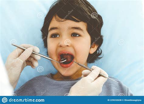 Cute Arab Boy Sitting At Dental Chair With Open Mouth During Oral