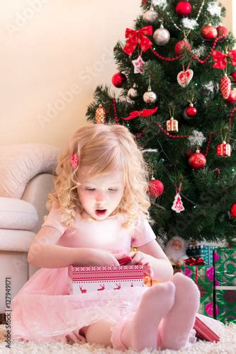 Девочка в розовом платье удивлённо открывает подарок Stock Photo And