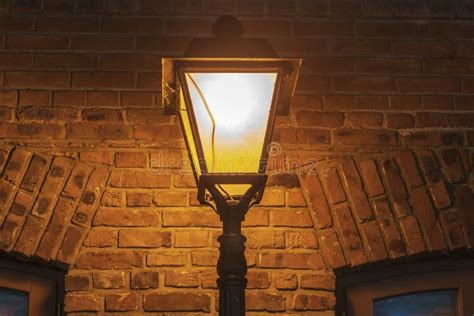 Lit Lamp Post Against A Textured Brick Wall At Night Stock Image