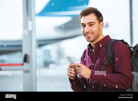 Cheerful Man Holding Smartphone And Smiling In Airport Stock Photo Alamy