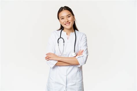 아시아 여성 의사 청진기가 달린 의료복을 입은 의사 가슴에 팔짱을 끼고 웃고 전문적인 흰색 배경 무료 사진