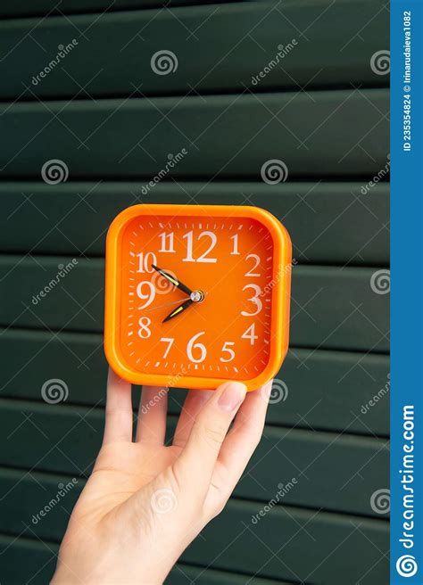 Orange Alarm Clock In A Womanand X27s Hand On Green Wooden Fence Stock
