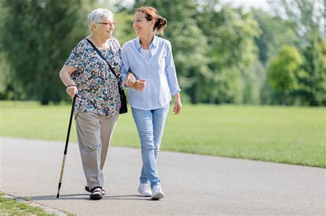 Happy Senior Woman And Caregiver Walking Outdoors Stock Photo