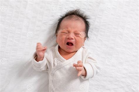 Crying And Angry Newborn Baby Boy Lying On White Bed At Homeinfant