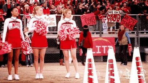 Cheerleaders In Red And White Outfits Stand Near Cones Holding Signs