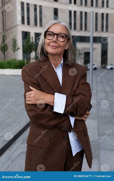 a slender gray haired business woman of mature years is dressed in an elegant brown suit on a
