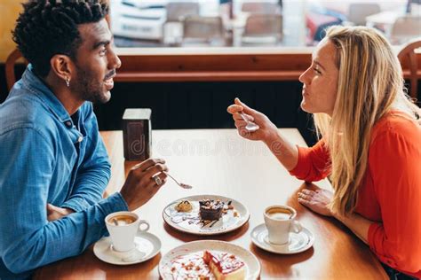 Interracial Couple Having Coffee And Cake Sitting At A Table In A