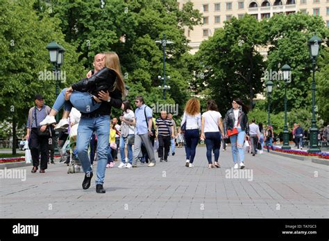 joyful man carrying blonde girl in his arms on a street people walking in alexander garden