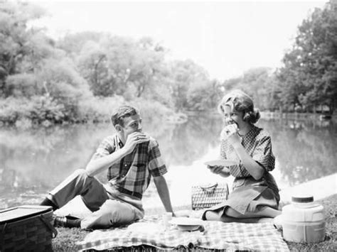Couple Seated On Checkered Tablecloth With Picnic Basket And Cooler