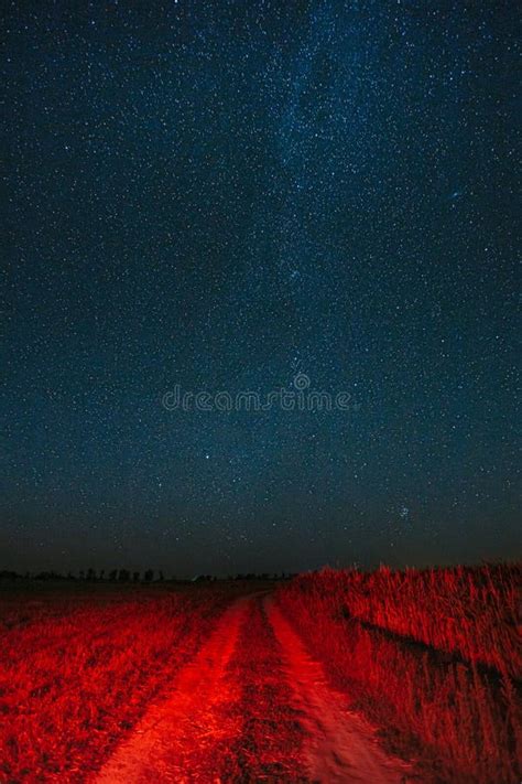 Night Starry Sky With Glowing Stars Above Country Road Is Lit In Red