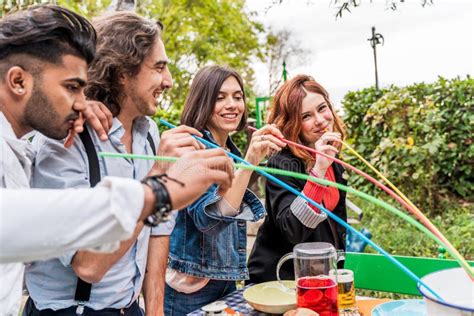 Group Of Multi Cultural Friends Having Fun At The Garden Party Sucking Beer From Colorful Straws