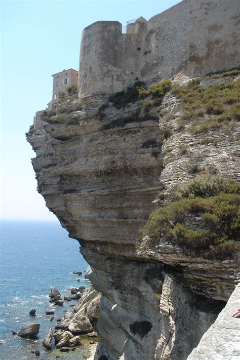 A Person Sitting On The Edge Of A Cliff Next To The Ocean With A Castle