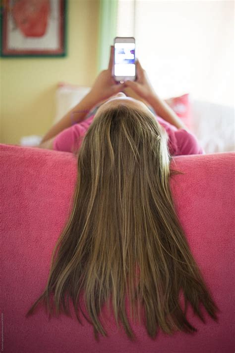Young Girl Laying On Her Bed Texting Long Hair Over The Side Of The
