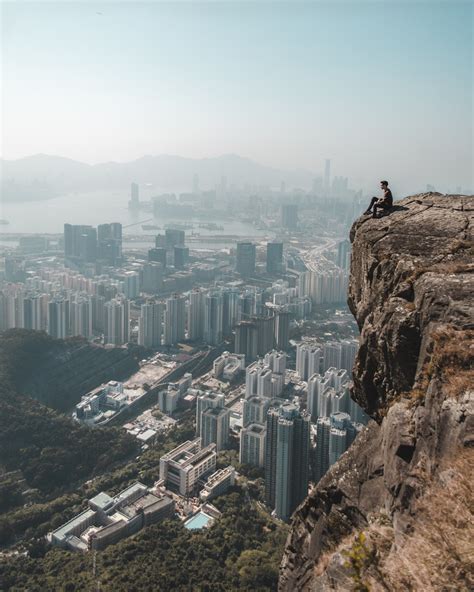 Person Sitting On Cliff Overlooking Cityscape At Daytime Photo Free