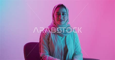 سيدة عربية سعودية خليجية محجبة، تقوم بجلسة تصوير مع إضاءة ملونة، تنظر إلى الكاميرا بإيماءات وجه