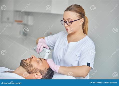 Charming Female Esthetician Treating Male Skin With Laser Device Stock